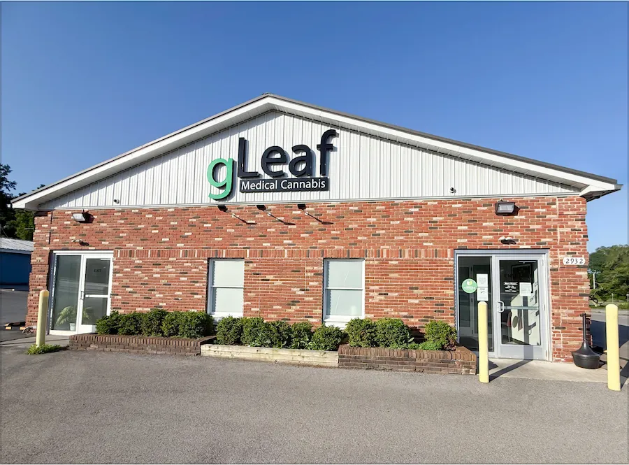 Front view of the gLeaf Medical Cannabis dispensary in Warren, Ohio. The building features a red brick exterior with a gray metal roof, trimmed hedges along the front, and the gLeaf logo above the main entrance door.